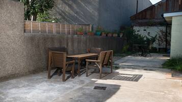 An outdoor patio with a wooden table and chairs, potted plants, and a concrete floor.