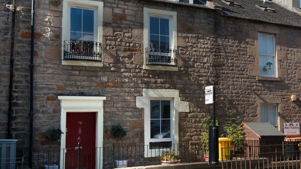 A stone building with a red door, multiple windows, and a balcony. - 7 Bedroom Townhouse (Edinburgh)