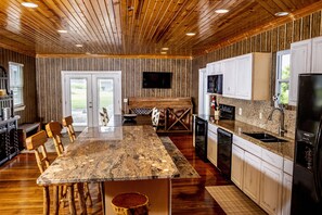 Une cuisine spacieuse dotée d’un grand îlot central, d’un plafond en bois et d’un téléviseur à écran plat fixé au-dessus de l’îlot.