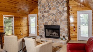 Ein gemütliches Blockhaus-Interieur mit Kamin aus Naturstein, Holzwänden und einem roten Ledersofa.