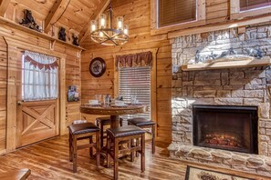 Cozy cabin-style room with a stone fireplace, wooden table, and chandelier.