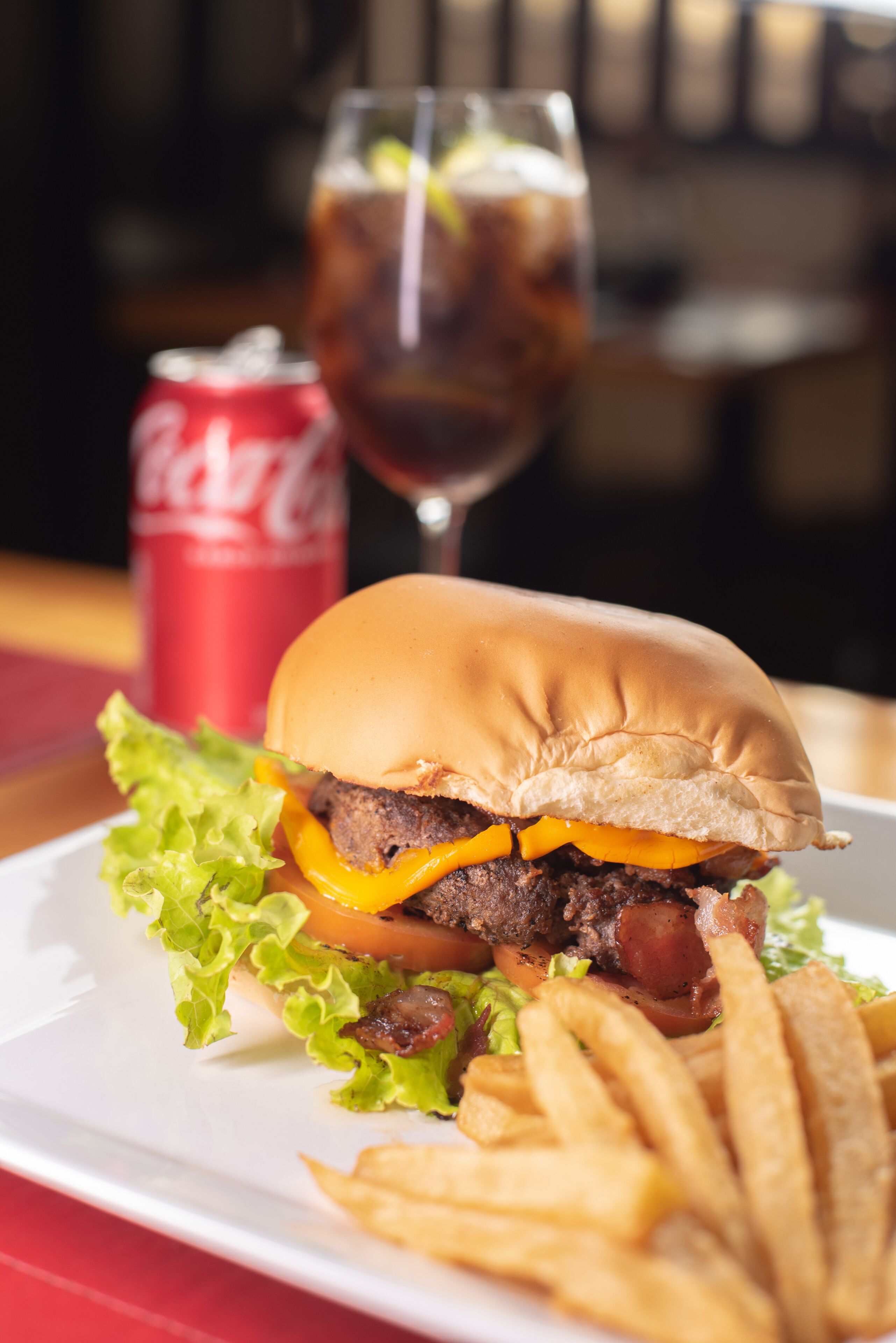 A burger with lettuce, tomato, and cheese, accompanied by French fries and a glass of soda.