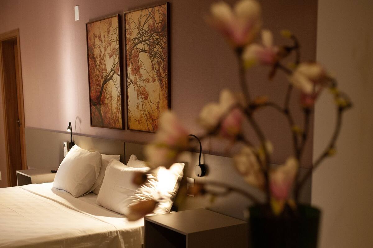 A bedroom with a bed, bedside table, and a vase with flowers.