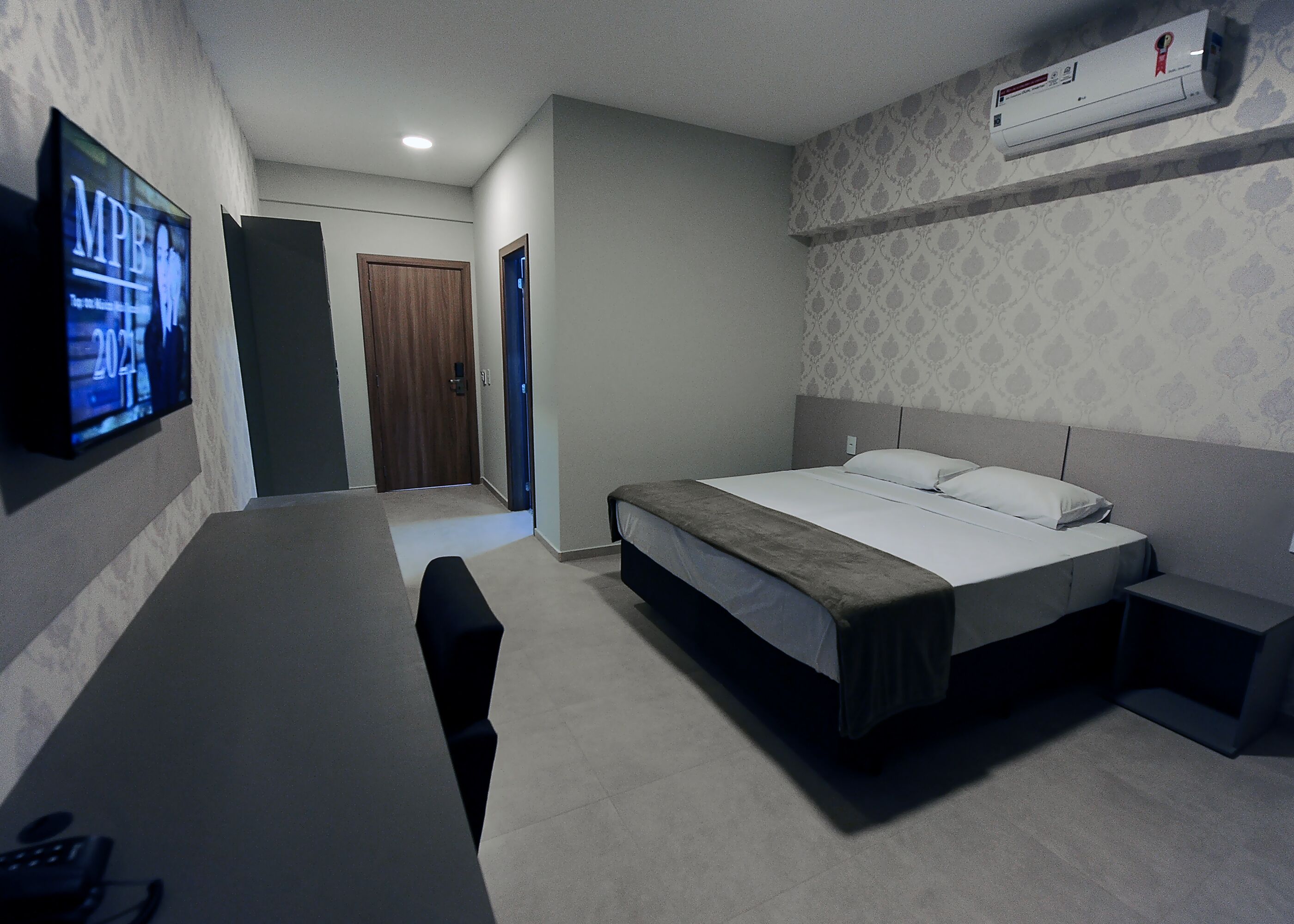 Een slaapkamer met een bed, nachtkastje en een aan de muur bevestigde televisie.