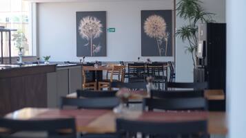 Ein moderner Essbereich mit Holztischen und -stühlen, einer großen Küstertopf-Pflanze und zwei Wandbildern mit Löwenzahnmotiven.