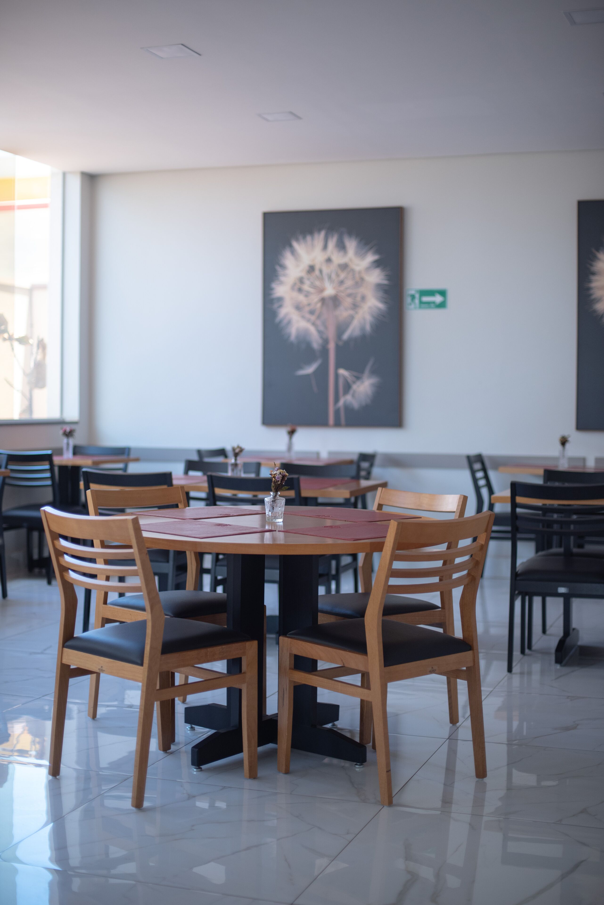 Un comedor con mesas y sillas de madera, un jarrón con flores y obras de arte en las paredes.