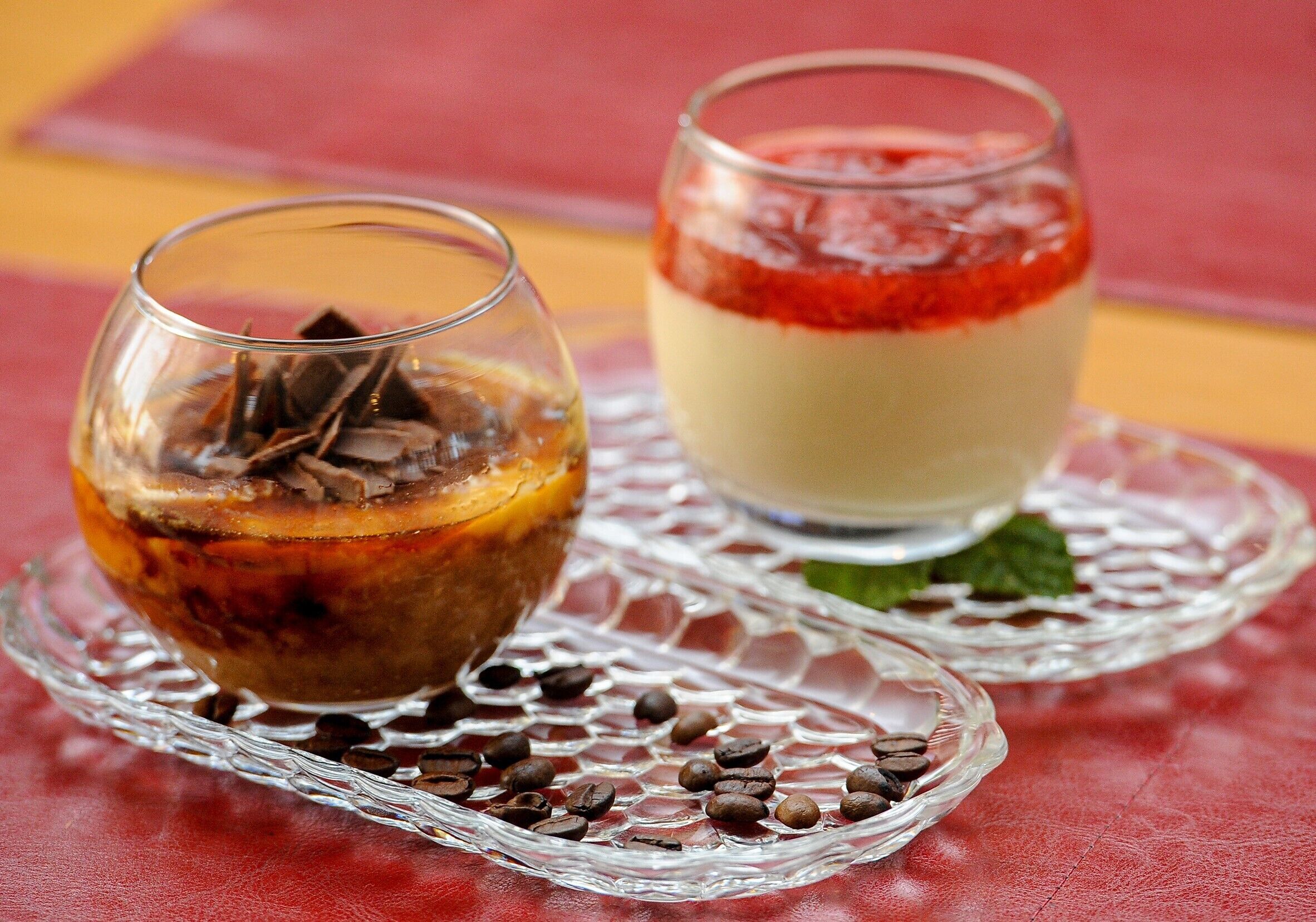 Dos postres sobre platos de vidrio transparente con granos de café esparcidos alrededor.