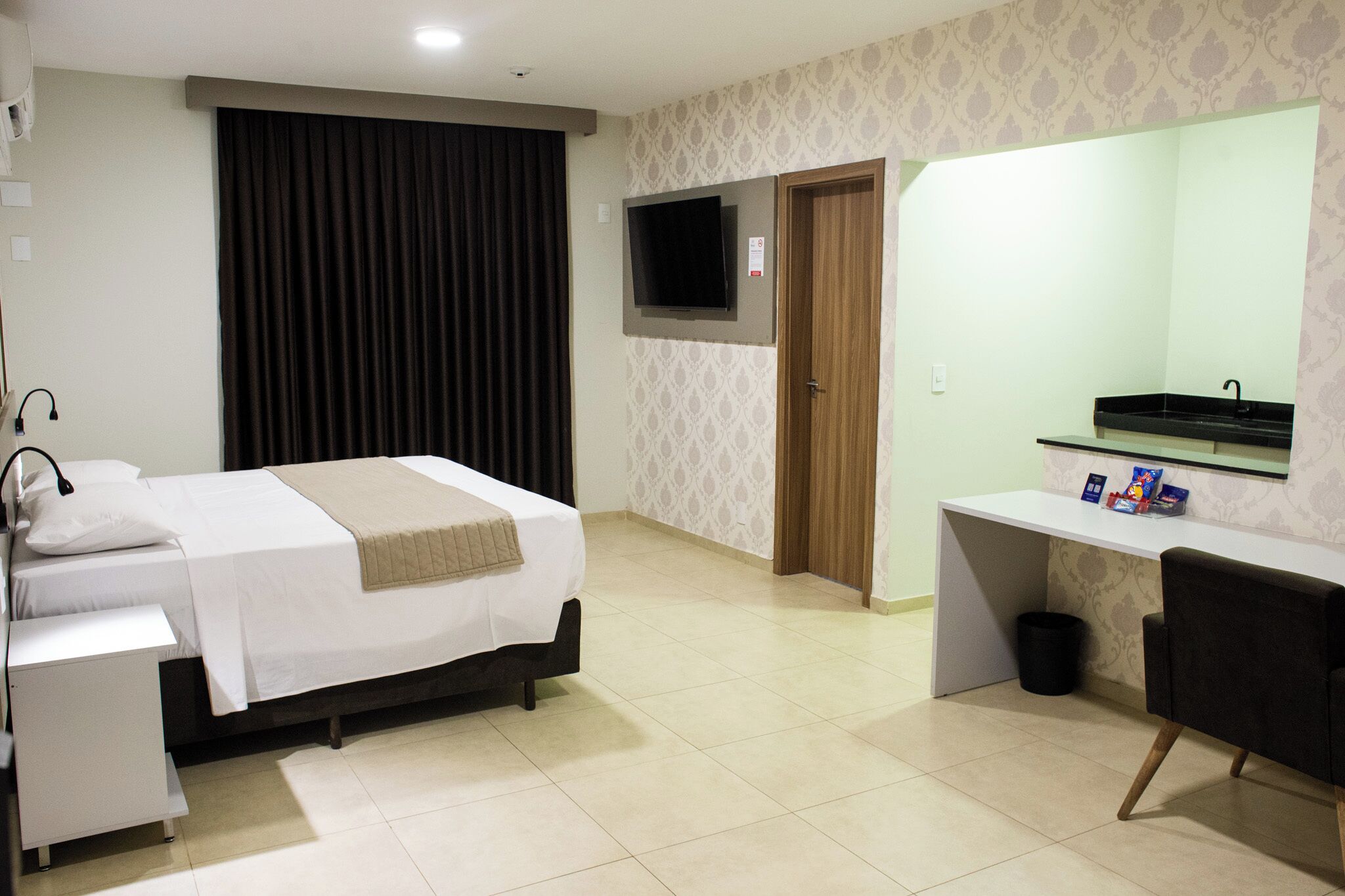 Quarto de hotel com cama, escrivaninha, televisão e banheiro.