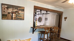 Een eethoek met een houten tafel en stoelen, een schilderij aan de muur, en een deur versierd met een krans.