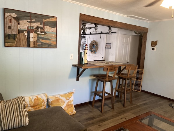 A dining area with a wooden table and chairs, a painting on the wall, and a door with a wreath.