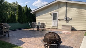 Een terras met een vuurkorf, tuinmeubilair en een groene omheining.
