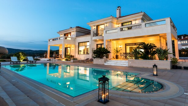 A modern two-story house with a swimming pool, outdoor seating, and a well-lit patio area. - East Coast Mansion (Ανάβυσσος)