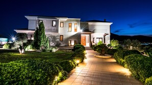 A modern two-story house with a well-lit driveway and landscaped garden. - East Coast Mansion (Ανάβυσσος)