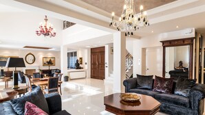 A spacious living area with a chandelier, a dining set, and a large mirror. - East Coast Mansion (Ανάβυσσος)