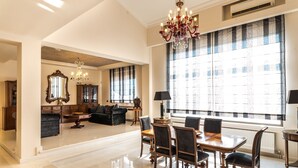 A spacious living room with a dining area, large windows, and a chandelier. - East Coast Mansion (Ανάβυσσος)