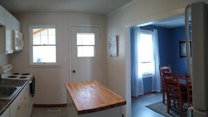 A kitchen with white cabinets, a wooden countertop, and a dining area with a blue wall and wooden chairs.