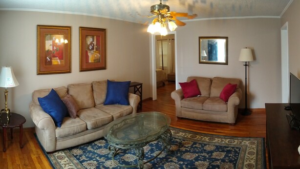 A living room with two sofas, a glass coffee table, a floor lamp, and a ceiling fan.
