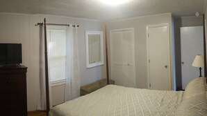 A bedroom with a bed, a dresser, a television, and a window with blinds.