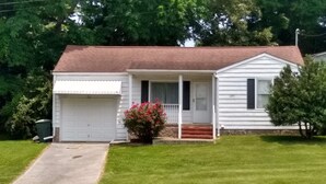 A single-story house with a garage, a front porch, and a small front yard with a flower bed.