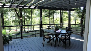 Eine überdachte Terrasse im Freien mit Tisch und Stühlen, umgeben von einem Geländer und Bäumen.