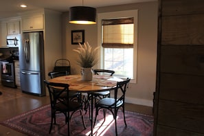 A kitchen with a dining table, chairs, a refrigerator, and a window with blinds.