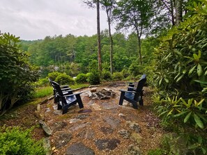 Zwei Adirondack-Stühle auf einem Steinweg, umgeben von üppigem Grün und Bäumen.