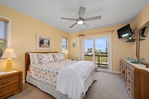 A bedroom with a bed, a ceiling fan, a TV, a dresser, and a balcony with a view. - The Dancing Sea Horse: Private Pool, Elevator, Spa (Kitty Hawk)