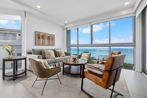 A modern living room with a large window overlooking the ocean, a sofa, two armchairs, and a coffee table. - Modern Oceanfront Getaway Apt. Azure – 716 (Noord)