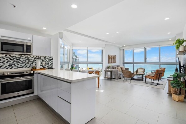 A modern kitchen with a central island, a dining area with a view, and a living space with a large window overlooking the ocean.