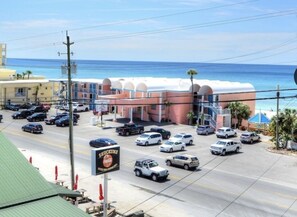 A parking lot with several cars, a building with a sign for 'SHOCKUMS', and a view of the ocean.