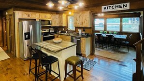 A rustic kitchen with wooden cabinets, a stainless steel refrigerator, a central island with stools, and a ceiling-mounted light fixture.
