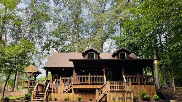 A rustic cabin with a porch, wooden stairs, and a fenced yard.