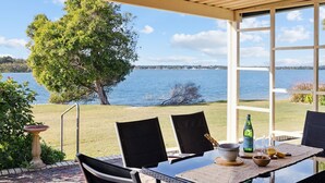 An outdoor dining area with a table, chairs, and a view of a lake. - Peninsula Court Unit 10 - Waterfront Unit with Pool & River Views - Holiday Yamba (YAMBA)