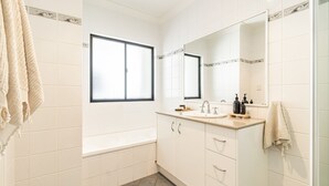 Une salle de bain avec une baignoire, un lavabo avec un miroir et des serviettes accrochées au mur.