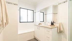A bathroom with a bathtub, a sink with a mirror, and towels on the wall. - Arcoola 2 - Views Over Main Beach - Holiday Yamba (Yamba)