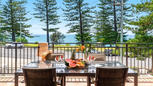 Un balcon avec une table dressée pour deux personnes, offrant une vue panoramique sur l’océan et la végétation.