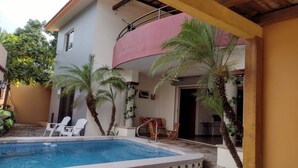 Ein Schwimmbecken mit gefliestem Rand, umgeben von Palmen und einer überdachten Terrasse.
