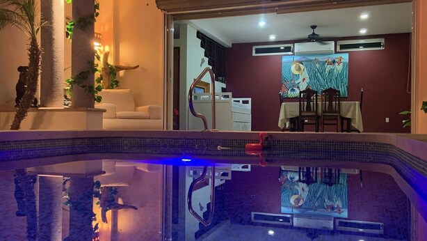 Ein Pool mit einer Fliesenverkleidung, ein Essbereich mit Tisch und Stühlen sowie ein Wandgemälde.