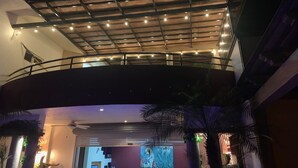 Ein überdachter Außenbereich mit einem gebogenen Balkon, Lichterketten und Palmen.