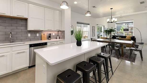 A modern kitchen with white cabinets, a large island, bar stools, and pendant lighting. - Gorgeous Townhome steps from the Brewery District! (Fort Collins)