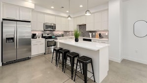 A modern kitchen with white cabinets, stainless steel appliances, and a central island with bar stools. - Gorgeous Townhome steps from the Brewery District! (Fort Collins)