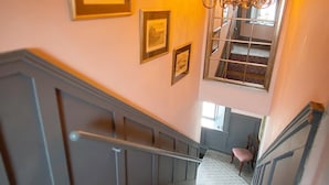 A staircase with a patterned carpet, a chandelier, and framed pictures on the wall. - @The Clock (Westport)