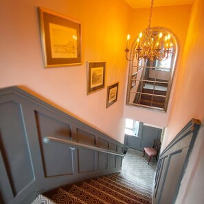 Staircase with a handrail, framed pictures, and a chandelier.