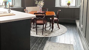 A kitchen with a central island, a dining table with chairs, a clock on the wall, and a window with a view of the outside. - @The Clock (Westport)