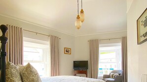 A bedroom with a large bed, a TV, a small table, and a chair. - @The Clock (Westport)