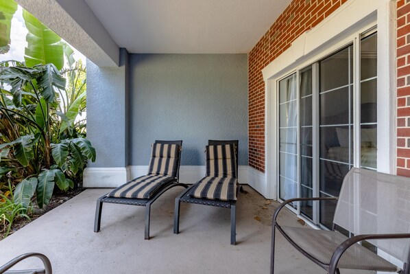 Two striped lounge chairs on a concrete patio with a brick wall and a large sliding glass door.