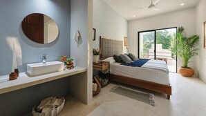 Un dormitorio moderno con una cama grande, un espejo redondo, un lavabo blanco y una planta en maceta.