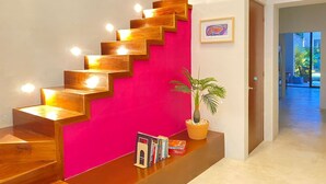 Una escalera con escalones de madera y una pared rosa brillante. Hay una planta en maceta y un pequeño estante con libros en la plataforma.
