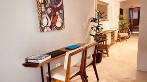 Un comedor con una larga mesa de madera, sillas blancas con cojines y una carpeta azul sobre la mesa.