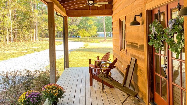 A wooden porch with a ceiling fan, wooden chairs, a bench, and a welcome mat. - Quaint Little Cabin with a view. (Abbeville)